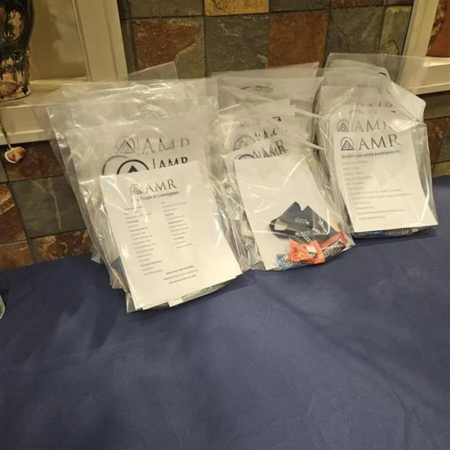 Multiple clear bags labeled with AMR branding, each containing brochures and giveaway items, displayed on a navy blue tablecloth.