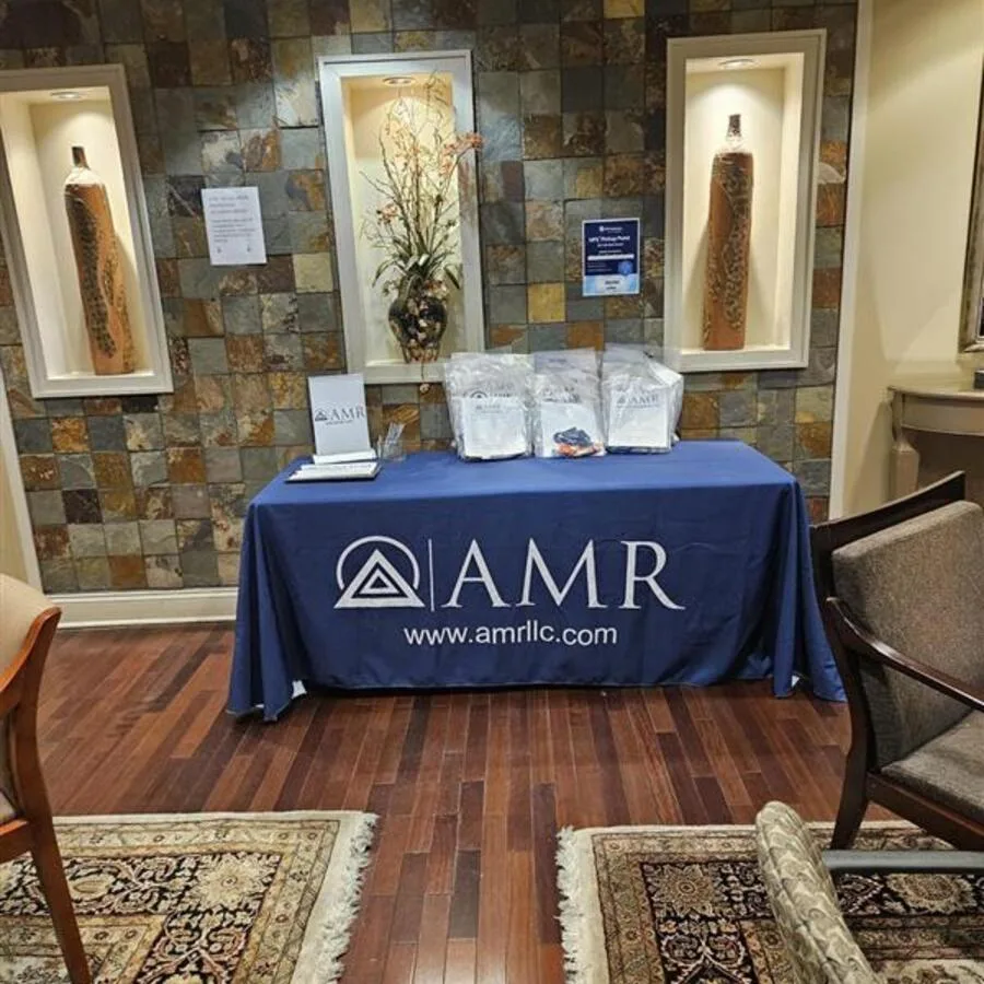 A full view of an AMR promotional setup in a lobby area, with giveaway bags and marketing materials arranged on a table against a decorative tile wall.