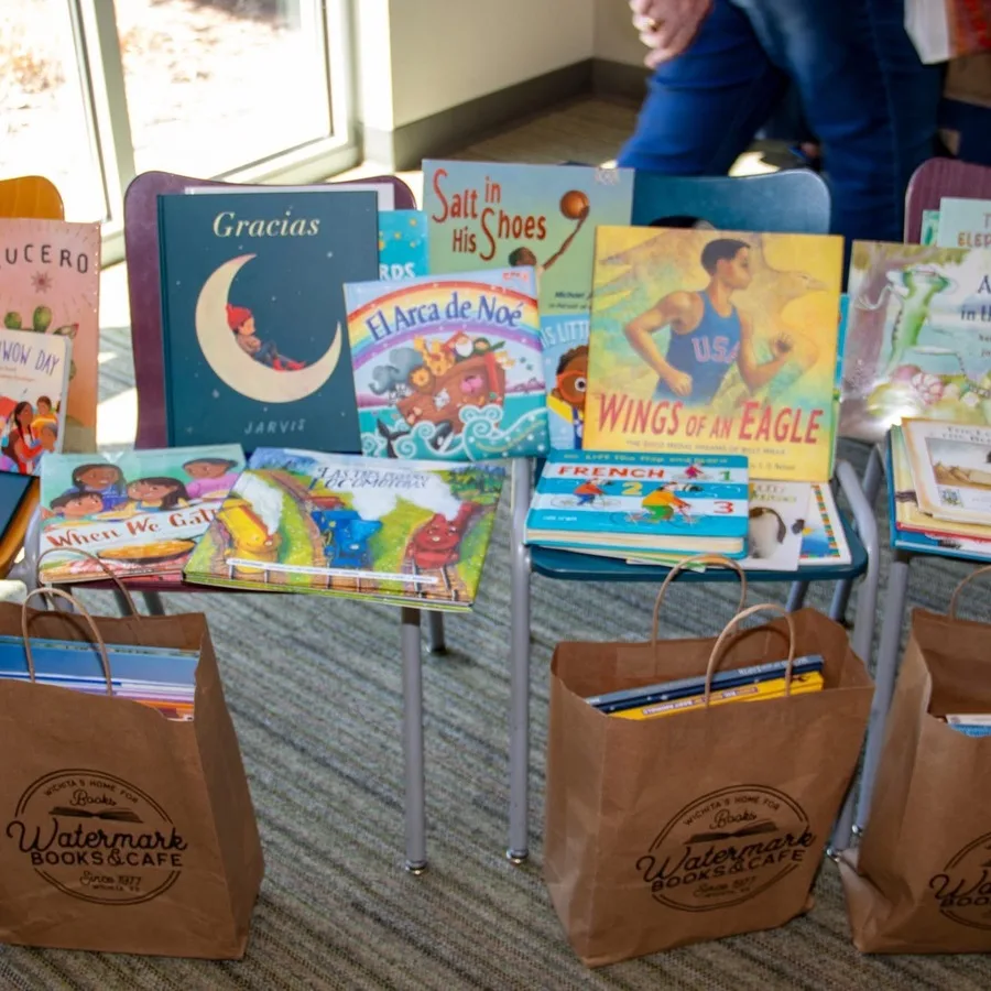 Close-up of the book donation table showcasing children’s books like “Gracias,” “Salt in His Shoes,” and “The Blessing Cup,” arranged upright and on stands. AMR-branded signage and bookmarks are placed around the books.