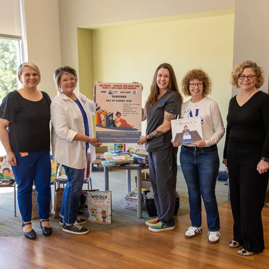 A wider angle of the book donation setup indoors, with AMR representatives standing near the table. Posters and books line the display area, highlighting the organization's community involvement.